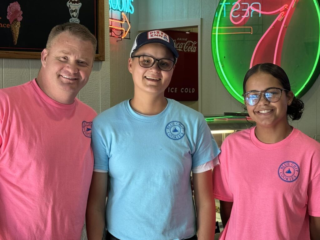 Three people smiling in a diner with neon signs